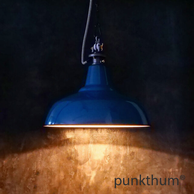 Blaue Emaillelampe, Industrielampe mit Stahlguss-Aufhängung und Textilkabel, eingeschaltet.