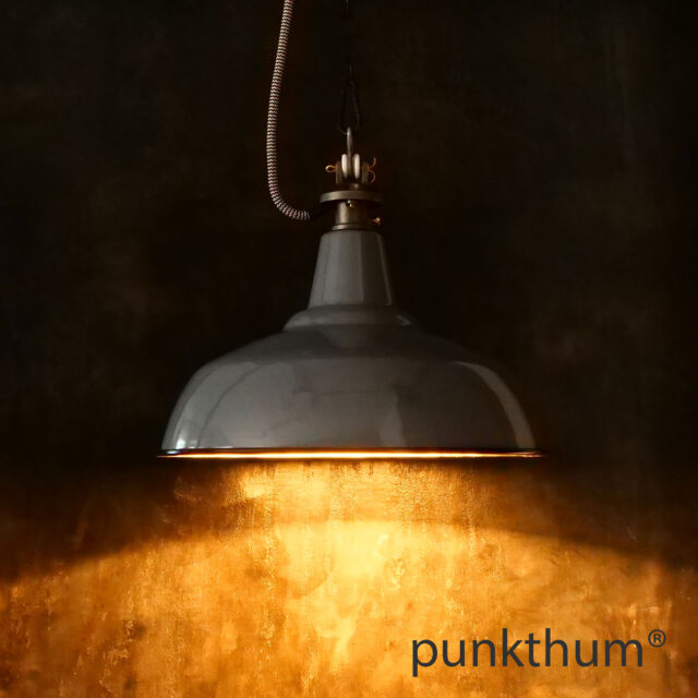 Graue Emaillelampe, Industrielampe mit Stahlguss-Aufhängung und Textilkabel, eingeschaltet.